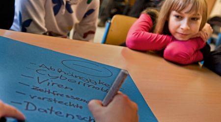 Zwei Kinder schauen auf eine Hand, die etwas auf einen blauen Zettel schreibt