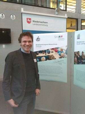 Timo Räker vor einem Plakat „Modellschule für Lernen mit digitalen Medien“