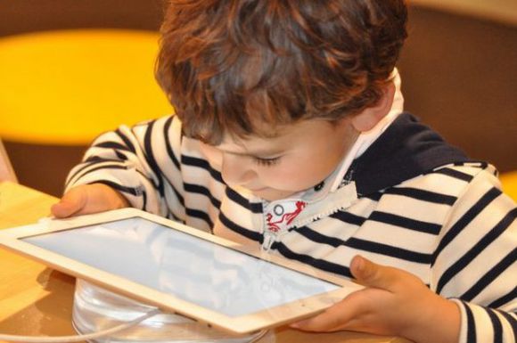 Ein kleiner Junge sitzt mit einem Tablet in den Händen am Tisch